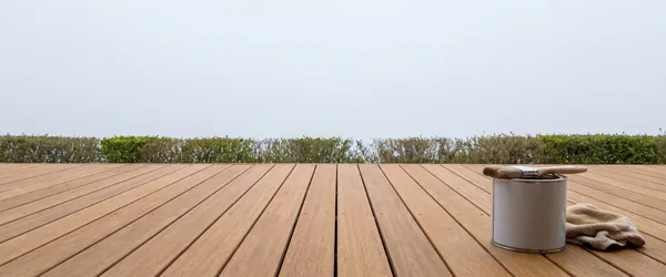 Oil can, brush and cloth on brown terrace decking. Vegetable-oil-based terrace oil soaks into the timber rather than leaving a surface film.