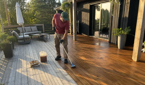A worker applies timber treatment along full board lengths, three boards at a time, to avoid visible overlaps.