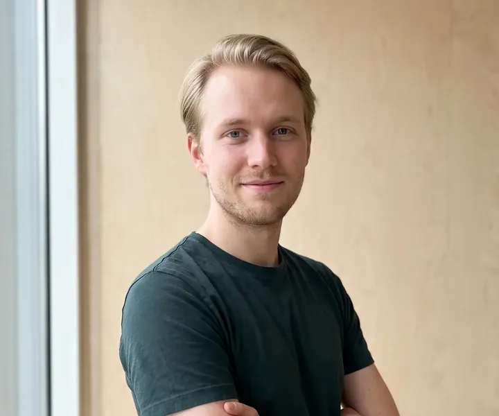 Joosep Ruusmaa tumerohelises T-särgis seisab käed rinnal ja keha kergelt küljega vineerseina ees, terrassilaud kinnitatakse roovile 5 x 60 mm terrassikruviga.