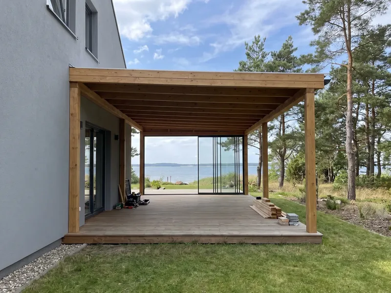 Uus puidust terrassikatus postidel halli maja terrassi kohal, kaugem külg on suletud klaasist liuguksedega ja nende taga paistab meri, Lohusalu sadam asub Lohusalu poolsaare idarannikul.