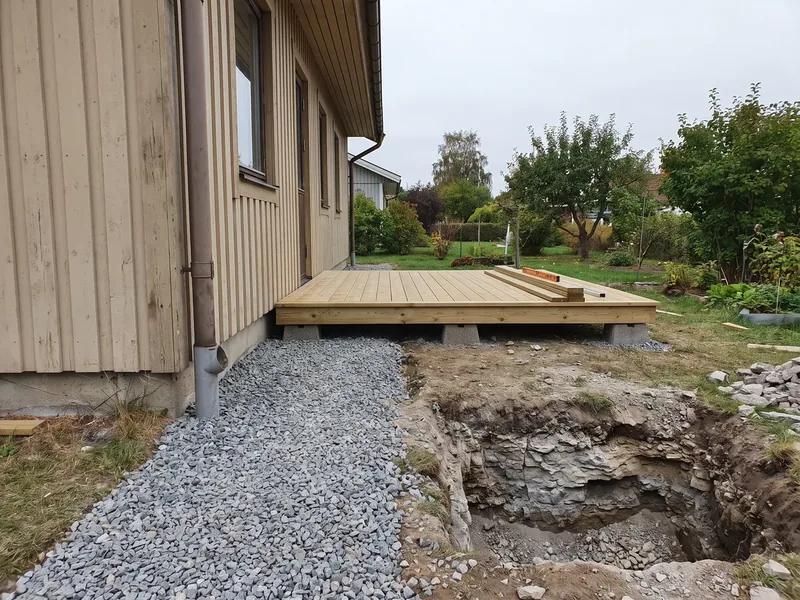 Väike immutatud männist terrass madalatel betoonplokkidel maja kõrval ja süvendi põhjas hall paekivi, betoonploki peale laotakse enne tala tõrvapapist riba, mis katkestab niiskuse tee betoonist puitu.